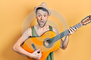 Young hispanic man playing classical guitar afraid and shocked with surprise and amazed expression, fear and excited face