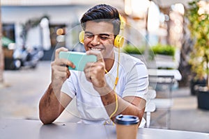 Young hispanic man playing video game drinking coffee at coffee shop terrace
