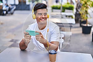 Young hispanic man playing video game drinking coffee at coffee shop terrace