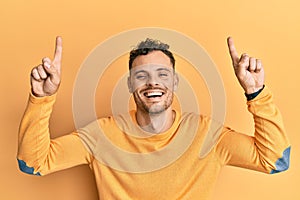 Young hispanic man pointing up with fingers smiling and laughing hard out loud because funny crazy joke