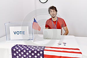 Young hispanic man at political election sitting by ballot making fish face with lips, crazy and comical gesture