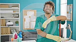 Young hispanic man professional cleaner holding mop smiling at office