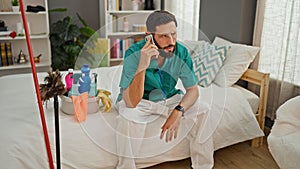 Young hispanic man professional cleaner talking on smartphone at bedroom
