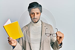 Young hispanic man reading a book and holding glasses depressed and worry for distress, crying angry and afraid