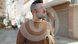 Young hispanic man with relaxed expression eating banana at street