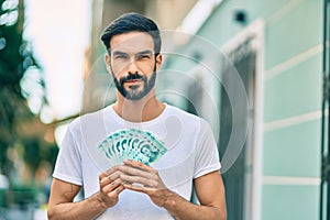 Young hispanic man with relaxed expression holding chinese yuan banknotes at the city