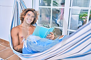 Young hispanic man relaxed reading book lying on the hammock at terrace