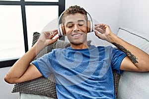 Young hispanic man relaxing sitting on the sofa wearing headphones at home