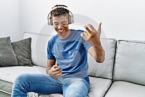 Young hispanic man relaxing sitting on the sofa wearing headphones at home