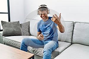 Young hispanic man relaxing sitting on the sofa wearing headphones at home