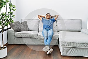 Young hispanic man relaxing sitting on the sofa wearing headphones at home