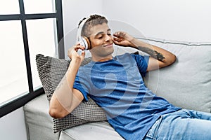 Young hispanic man relaxing sitting on the sofa wearing headphones at home