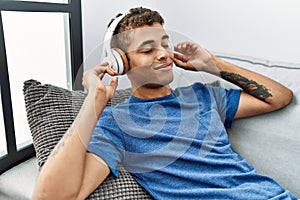 Young hispanic man relaxing sitting on the sofa wearing headphones at home