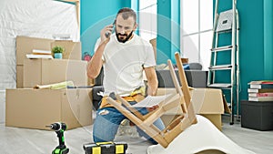 Young hispanic man repairman talking on smartphone reading instructions at new home