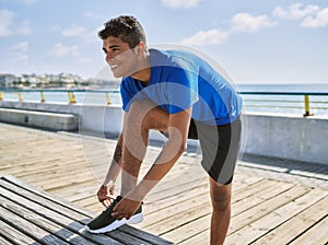 Young hispanic man resting tying shoes laces outdoors