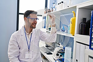 Young hispanic man scientist looking test tube at laboratory