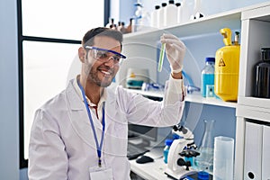 Young hispanic man scientist looking test tube at laboratory
