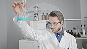 Young hispanic man scientist looking test tube at laboratory