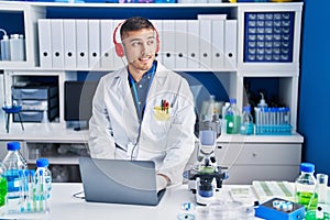 Young hispanic man scientist using laptop and headphones at laboratory