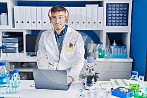 Young hispanic man scientist using laptop and headphones at laboratory