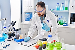 Young hispanic man scientist write on report holding bottle at laboratory