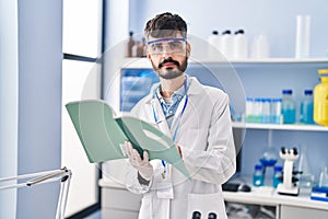 Young hispanic man scientist writing on notebook working at laboratory
