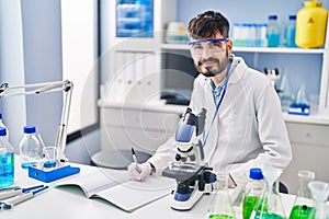Young hispanic man scientist writing on notebook working at laboratory