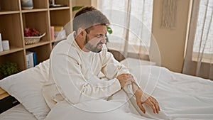 Young hispanic man scratching arm for itchy sitting on bed at bedroom