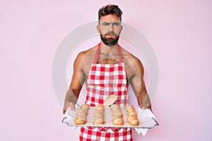 Giovane ispanico uomo logorante panettiere uniforme possesso domestico pane facce ridicolo 