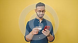 Young hispanic man shopping online with smartphone over isolated yellow background