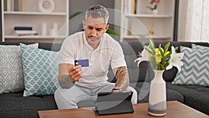 Young hispanic man shopping with touchpad and credit card at home