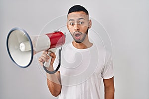 Young hispanic man shouting through megaphone scared and amazed with open mouth for surprise, disbelief face