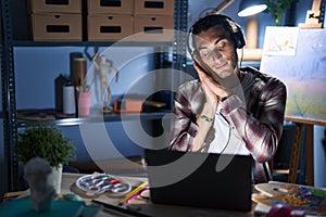 Young hispanic man sitting at art studio with laptop late at night sleeping tired dreaming and posing with hands together while