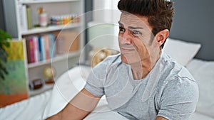 Young hispanic man sitting on bed scared at bedroom