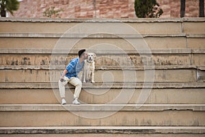 Young Hispanic man, sitting on big cement stairs giving a kiss to his dog in loving and tender attitude. Concept, dogs, pets,