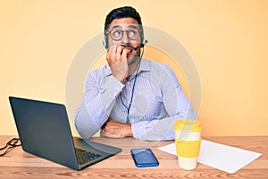 Young hispanic man sitting at the desk wearing operator headset at the call center office looking stressed and nervous with hands