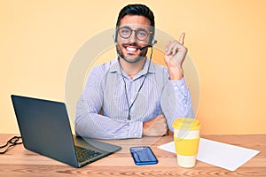 Young hispanic man sitting at the desk wearing operator headset at the call center office smiling happy pointing with hand and