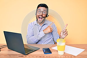 Young hispanic man sitting at the desk wearing operator headset at the call center office smiling and looking at the camera