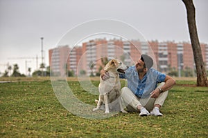 Young Hispanic man, sitting on the grass hugging his dog and looking at him very tenderly. Concept, dogs, pets, animals, friends
