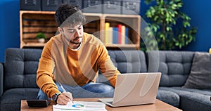 Young hispanic man sitting on sofa teleworking at home