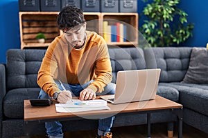 Young hispanic man sitting on sofa teleworking at home