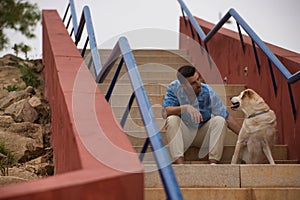 Young Hispanic man, sitting on stairs next to his dog while talking with him in a loving and tender attitude. Concept, dogs, pets