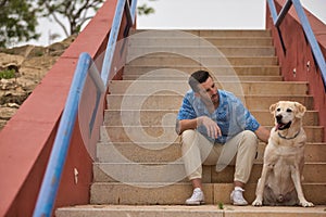Young Hispanic man, sitting on stairs next to his dog while talking with him in a loving and tender attitude. Concept, dogs, pets