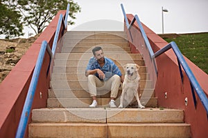 Young Hispanic man, sitting on stairs next to his dog while talking with him in a loving and tender attitude. Concept, dogs, pets