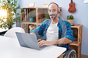 Young hispanic man sitting on wheelchair teleworking at home