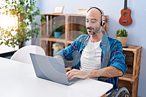 Young hispanic man sitting on wheelchair teleworking at home