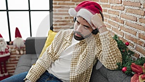 Young hispanic man sleeping on sofa wearing christmas hat at home