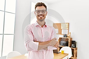 Young hispanic man smiling confident with arms crossed gesture at office