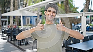 Young hispanic man smiling confident doing ok sign with thumbs up at coffee shop terrace