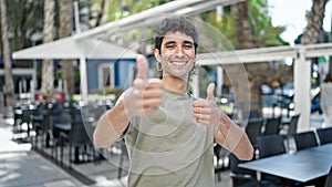 Young hispanic man smiling confident doing ok sign with thumbs up at coffee shop terrace